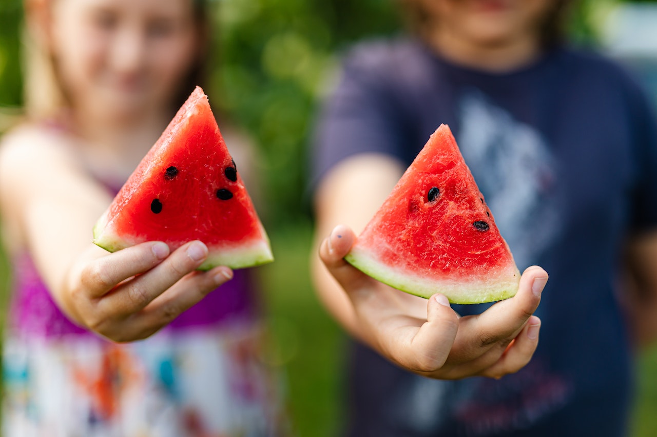Two young kids each holding a piece of watermelon. 