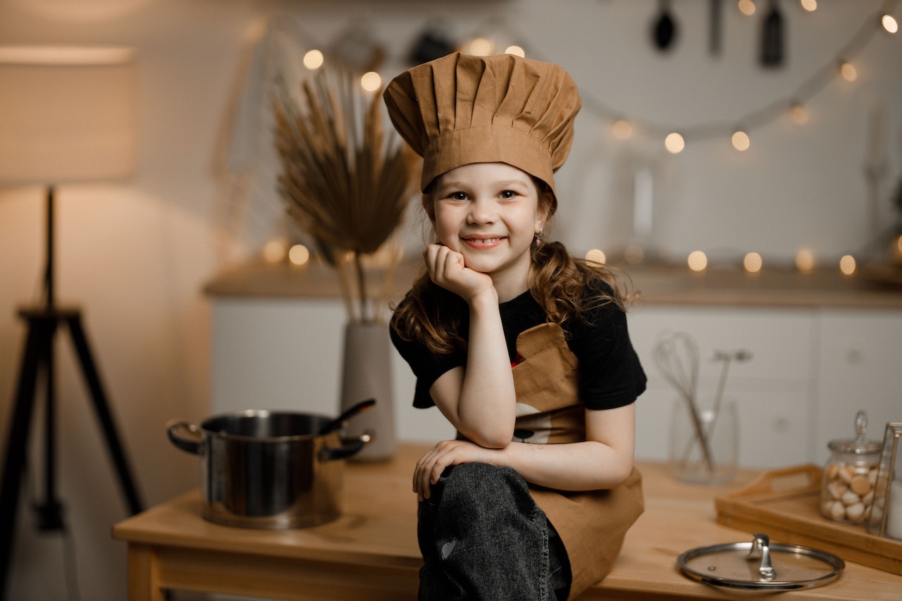 Toddler dressed up as chef sitting on kitchen table.