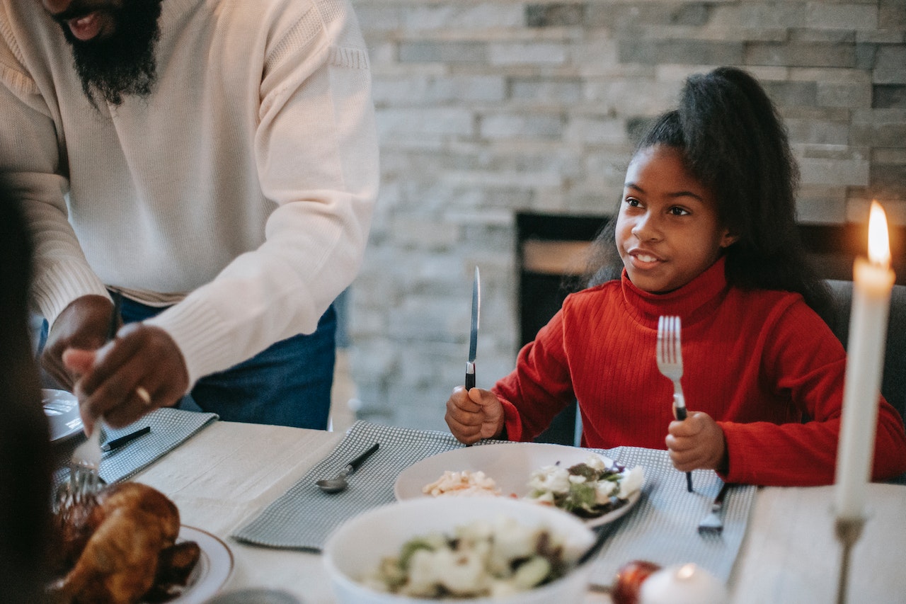 Happy young girl sitting at table with family during Thanksgiving dinner.